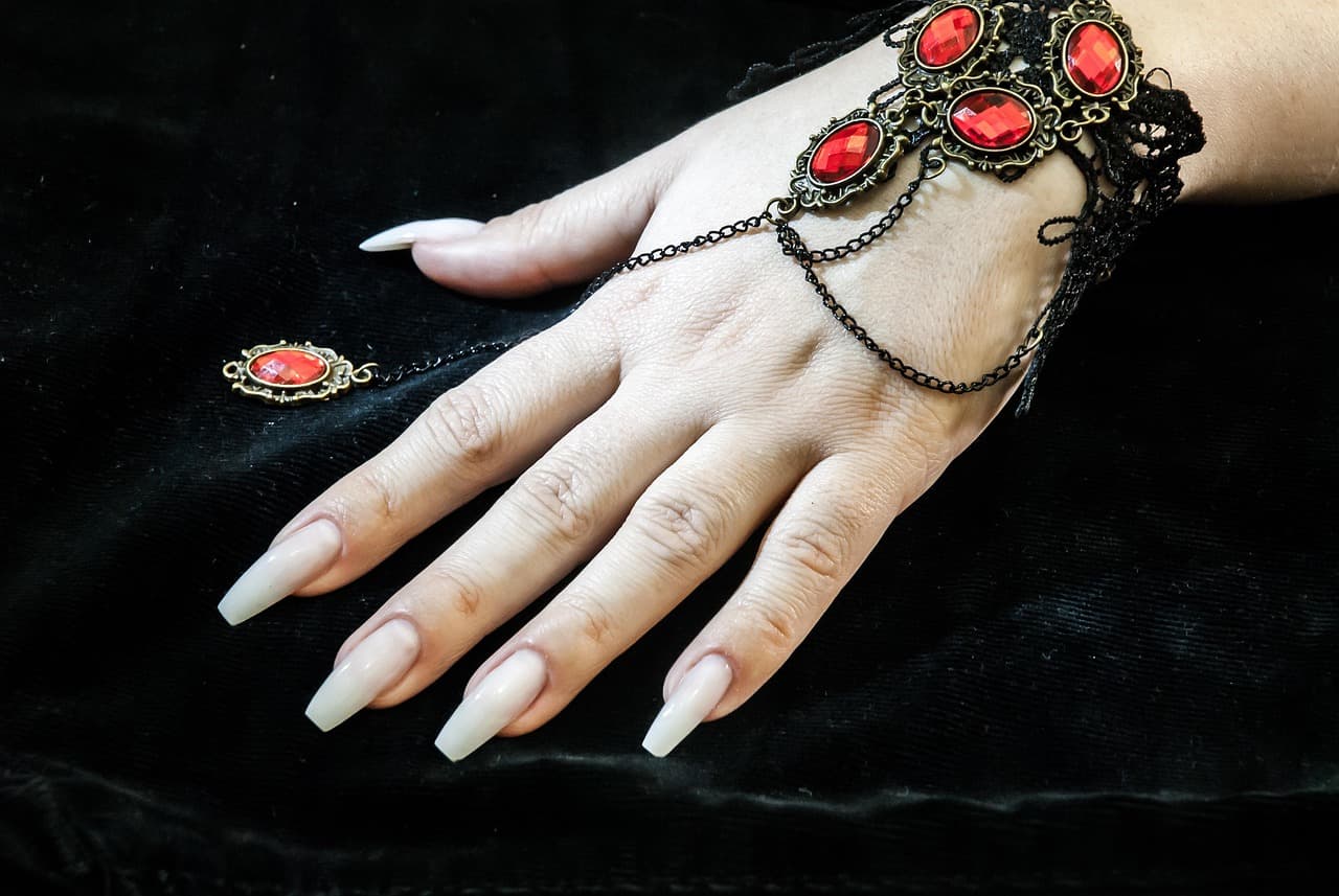 Long white coffin nails with a jewelled bracelet on black velvet