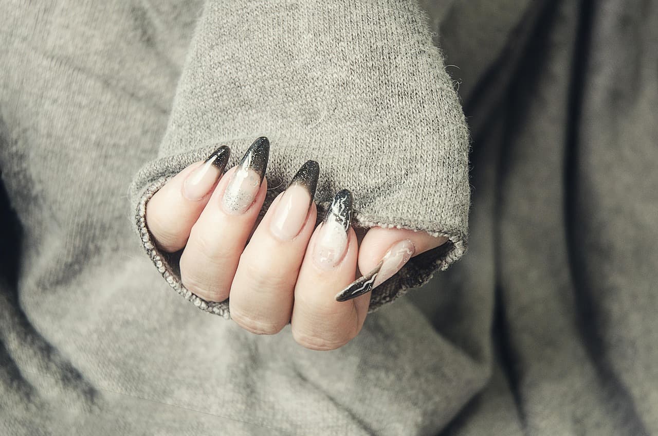 Long almond acrylic nails with dark tips, against a grey jumper