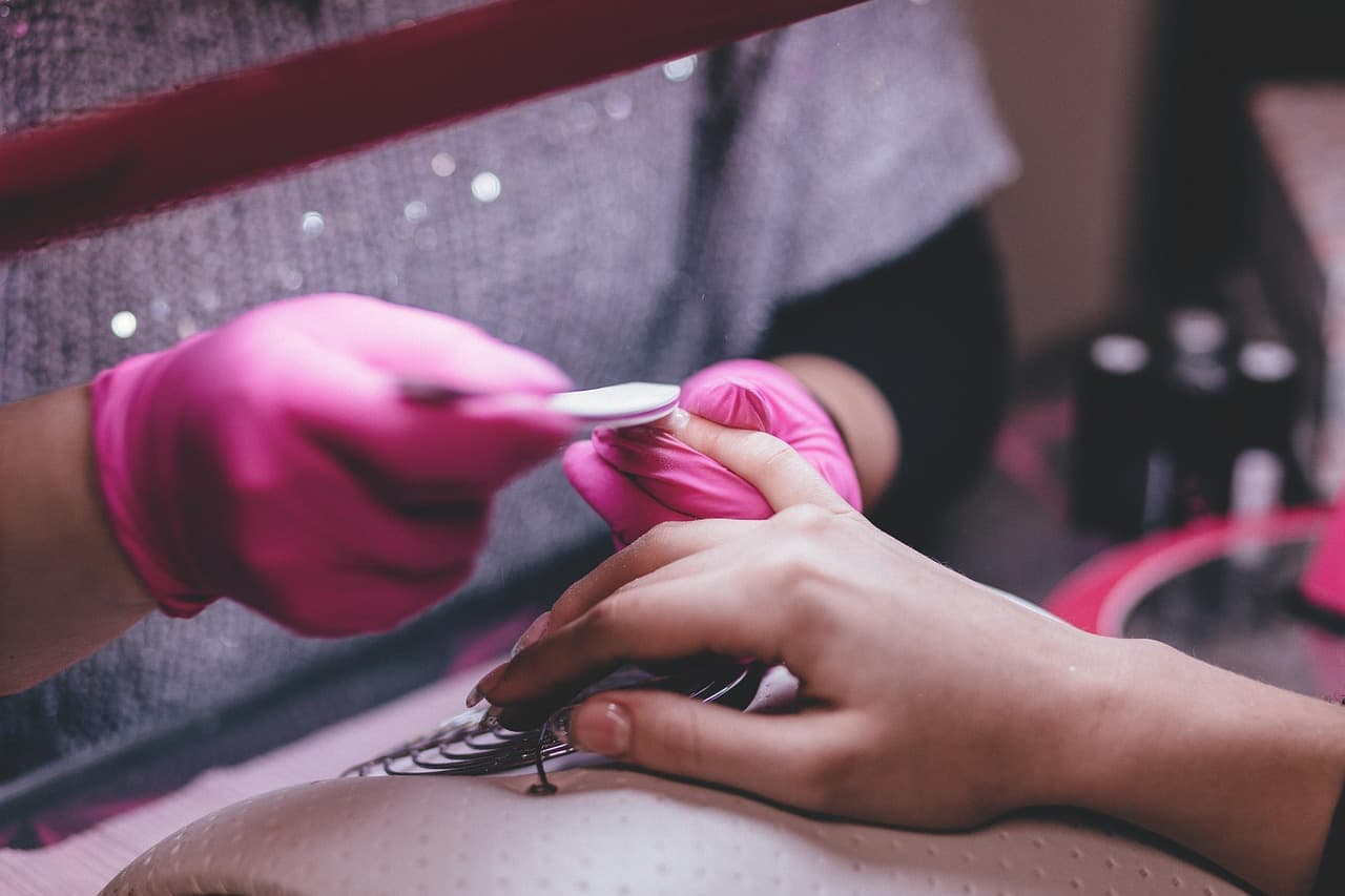 Nail technician in pink gloves filing a client’s nails